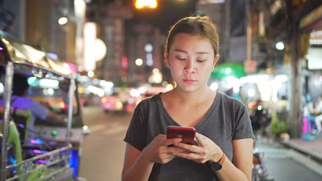 亚洲女孩在夜城的街道上使用手机视频素材