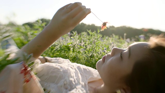 女孩躺在绿色的田野里，用鼻子闻着花香。视频素材