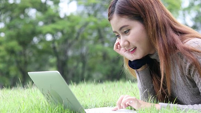 快乐的女学生带着笔记本电脑在公园里，摄影车拍摄视频素材