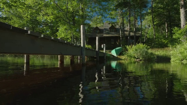 潘从左到右从码头上的湖到两层小屋，湖或度假屋在bg。独木舟在岸上。树。视频素材