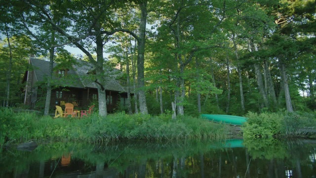 潘右向左从码头上的湖到两层小屋，湖或度假屋在bg。独木舟在岸上。树。视频素材