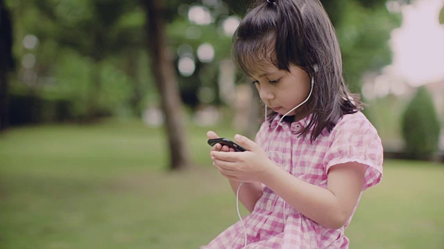 一个小女孩坐在泰国的公园里，戴着耳机听播客视频素材