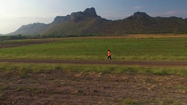 鸟瞰图的妇女在农村道路上奔跑在日落在山区视频下载