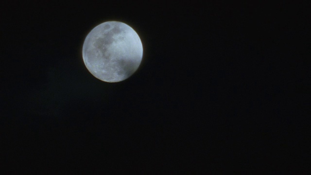 乌云在夜空中一轮明亮的满月前飘荡。视频素材