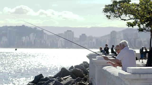 老人在海边城市的阳台上钓鱼，背景是树木。视频素材