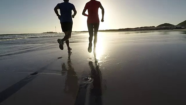 一对老年夫妇在美丽的海滩上慢跑，夕阳西下视频素材