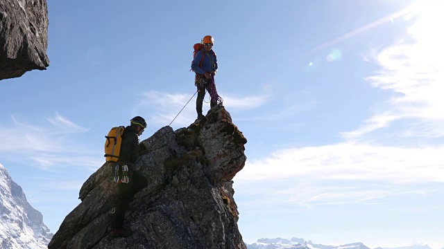 男性登山运动员攀登岩石的顶峰，下面是山脉视频素材