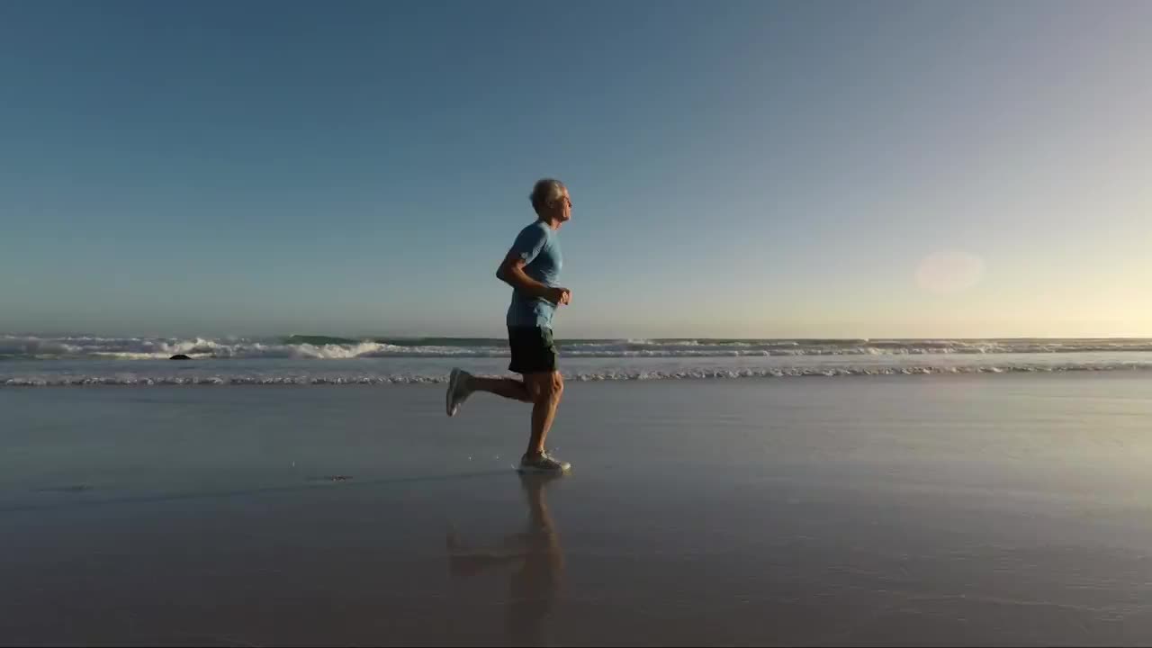 夕阳西下，一位老人在美丽的海滩上慢跑视频素材