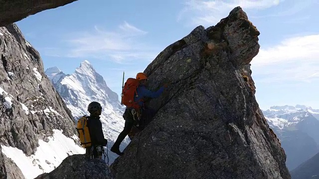 男性登山运动员攀登岩石的顶峰，下面是山脉视频素材