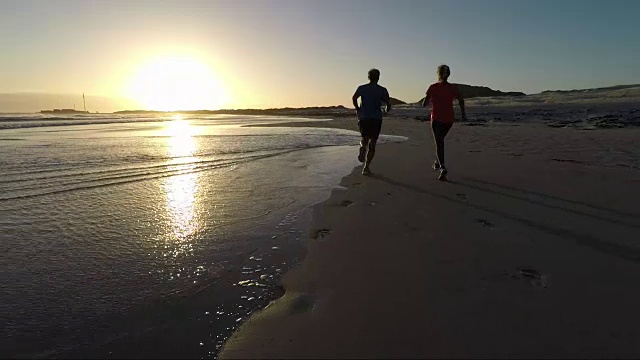 一对老年夫妇在美丽的海滩上慢跑，夕阳西下视频素材