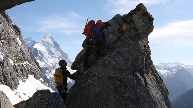 男性登山运动员攀登岩石的顶峰，下面是山脉视频素材