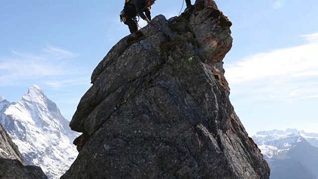 男性登山运动员攀登岩石的顶峰，下面是山脉视频素材