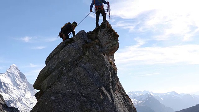 男性登山运动员攀登岩石的顶峰，下面是山脉视频素材