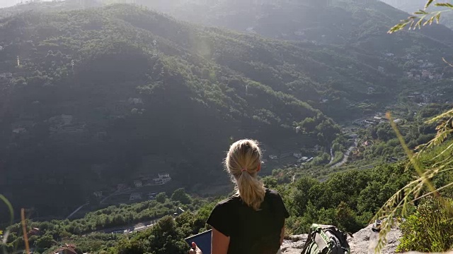 女性徒步旅行者在山谷上方的岩石上放松，用数码平板电脑视频素材