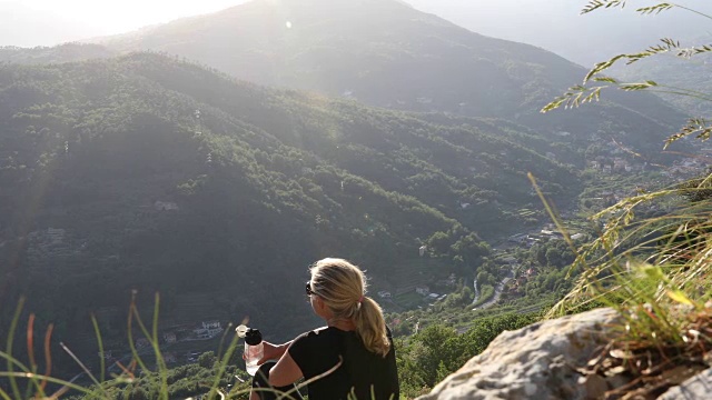 女性徒步旅行者在山谷上方放松，喝着水视频素材