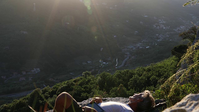 男性徒步旅行者在山谷上方放松，用着数码平板电脑视频素材