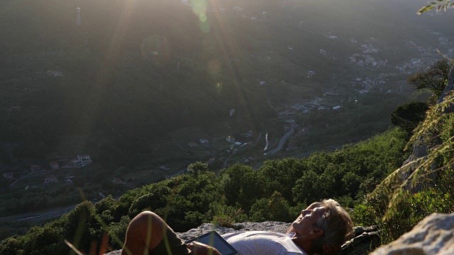 男性徒步旅行者在山谷上方放松，用着数码平板电脑视频素材