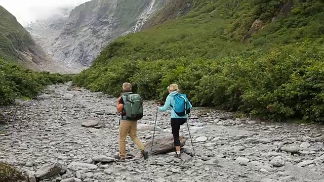 徒步旅行的夫妇沿着河床经过瀑布视频素材