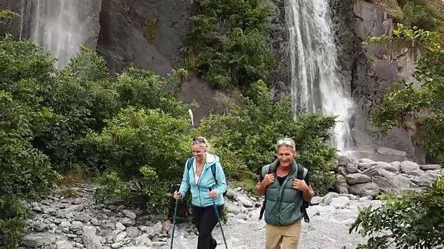 徒步旅行的夫妇沿着河床经过瀑布视频素材