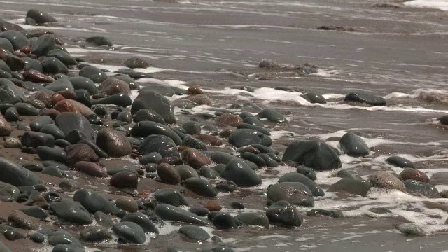 海滩或海岸上的岩石或石头的中等角度。可能是湖泊或海洋。砂可见。视频素材