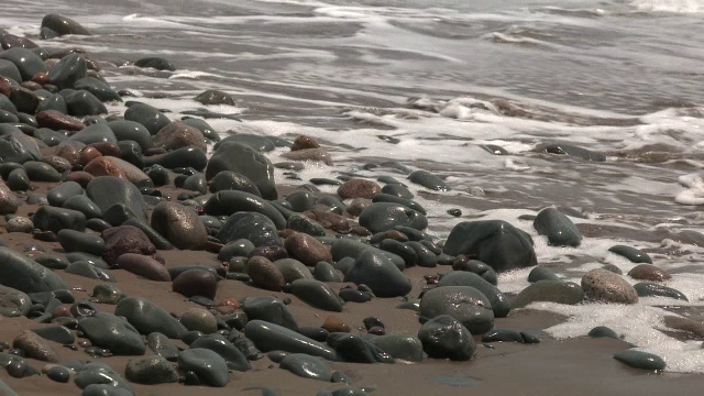 海滩或海岸上的岩石或石头的中等角度。可能是湖泊或海洋。砂可见。视频素材