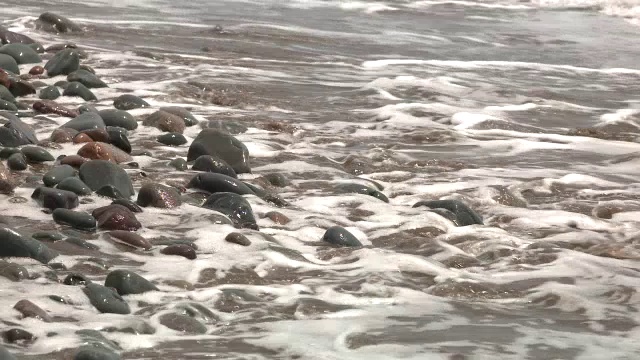 海滩或海岸上的岩石或石头的中等角度。可能是湖泊或海洋。砂可见。视频素材