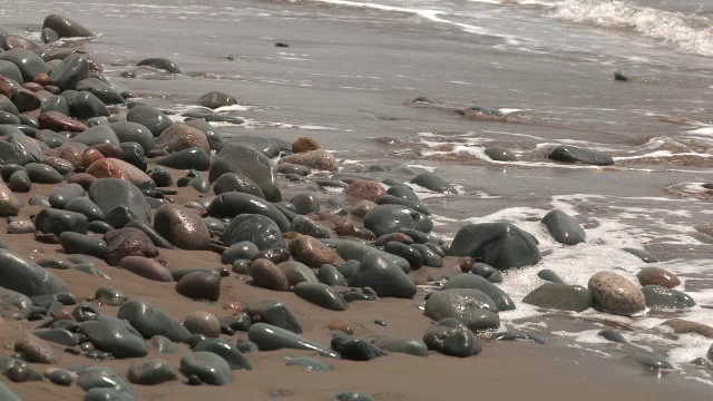 海滩或海岸上的岩石或石头的中等角度。可能是湖泊或海洋。砂可见。视频素材