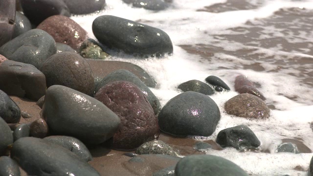 靠近海滩上的岩石或石头的角度。可能是湖泊或海洋。砂可见。视频素材