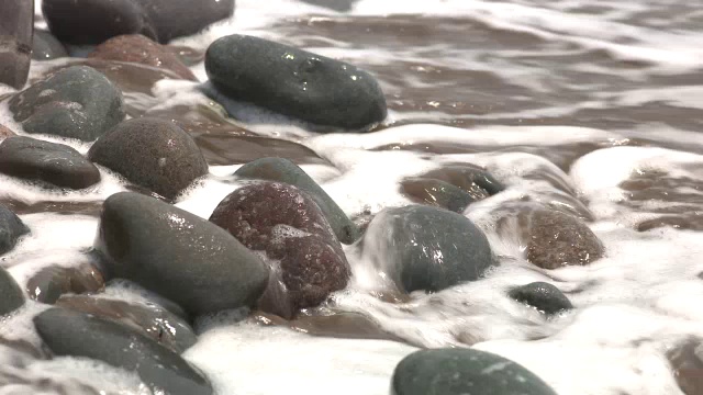 靠近海滩上的岩石或石头的角度。可能是湖泊或海洋。砂可见。视频素材