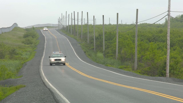 广角乡村道路。道路两旁可见围栏、电线杆和电线。汽车驾驶可见。警车可见。视频素材