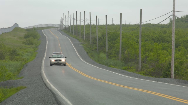 广角乡村道路。道路两旁可见围栏、电线杆和电线。汽车驾驶可见。警车可见。视频素材