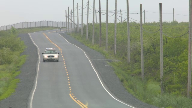 广角乡村道路。道路两旁可见围栏、电线杆和电线。汽车驾驶可见。警车可见。视频素材