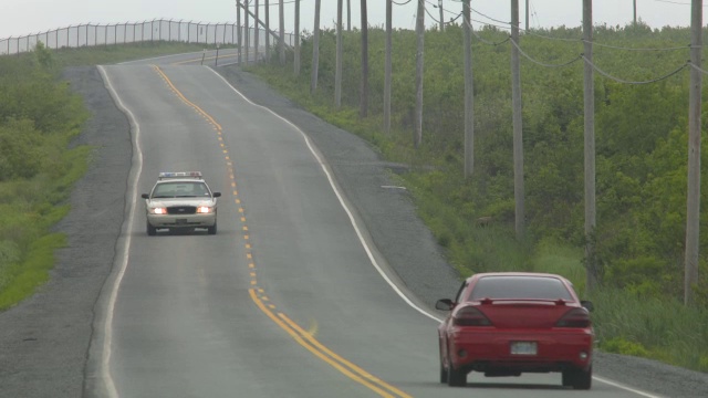 广角乡村道路。道路两旁可见围栏、电线杆和电线。汽车驾驶可见。警车可见。视频素材