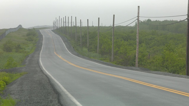 广角乡村道路。道路两旁可见围栏、电线杆和电线。汽车驾驶可见。警车可见。下雨了。视频素材