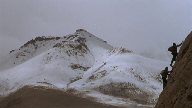 右泛越过雪山，两个人爬一个陡峭的岩石坡。视频素材