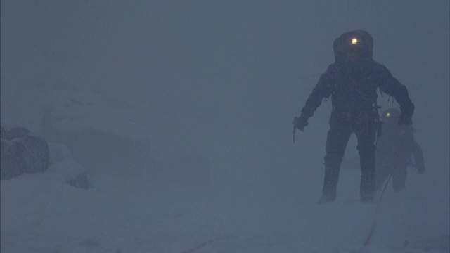 被绳子绑住的登山者在暴风雪中挣扎，一名登山者跌倒在镜头前。视频素材