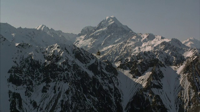 一架直升机飞过崎岖的、积雪覆盖的山峰的鸟瞰图。视频素材