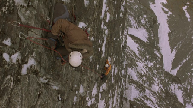 一名登山者把钩子挂在岩壁上，然后对另一名登山者大喊。视频素材