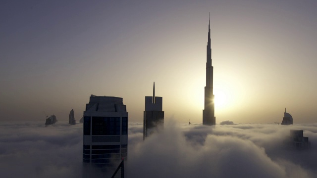 当太阳在迪拜的哈利法塔(Burj Khalifa)后面升起时，一层一层的雾在摩天大楼之间飘过视频素材