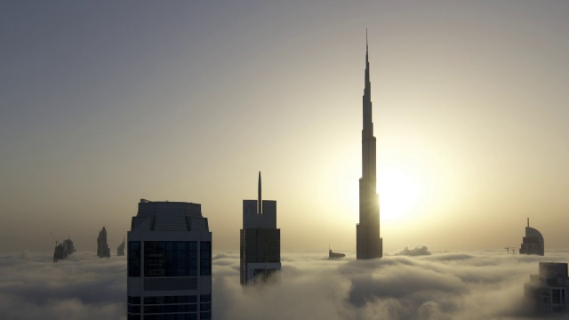 当太阳在迪拜的哈利法塔(Burj Khalifa)后面升起时，一层一层的雾在摩天大楼之间飘过视频素材