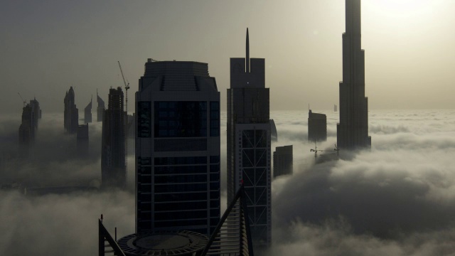 当太阳在迪拜的哈利法塔(Burj Khalifa)后面升起时，一层一层的雾在摩天大楼之间飘过视频素材