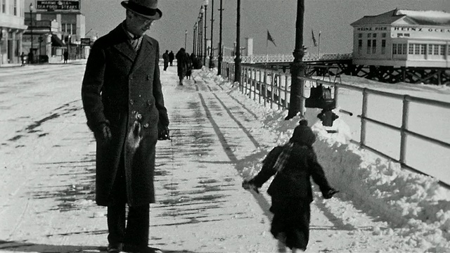 1936年，新泽西州大西洋城，黑白广角镜头，蹒跚学步的孩子拿着雪球追逐父亲/向父亲扔雪球视频素材