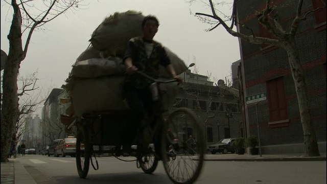 一名男子骑着装满包包的三轮自行车经过繁忙的十字路口/中国上海视频素材