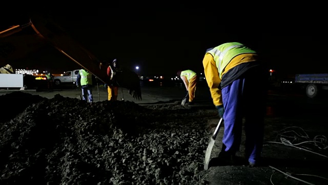 南非开普敦，挖掘机和工人们晚上在建筑工地上用铲子挖掘旧道路视频素材