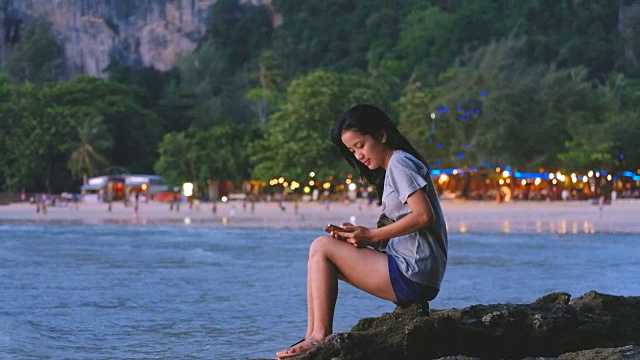 亚洲年轻女子在海滩上拿着手机视频素材