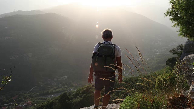 雄性徒步旅行者下到山谷上方的岩石高处视频素材