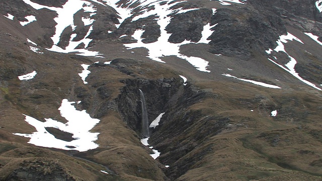 南乔治亚岛，福克兰群岛，英国海外领土，瀑布流入峡谷，棕色山坡上的雪片视频素材