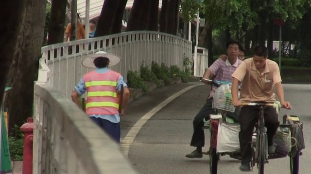 中国深圳，当车辆和骑自行车的人经过的时候，女性城市工人在街道旁边扫地视频素材