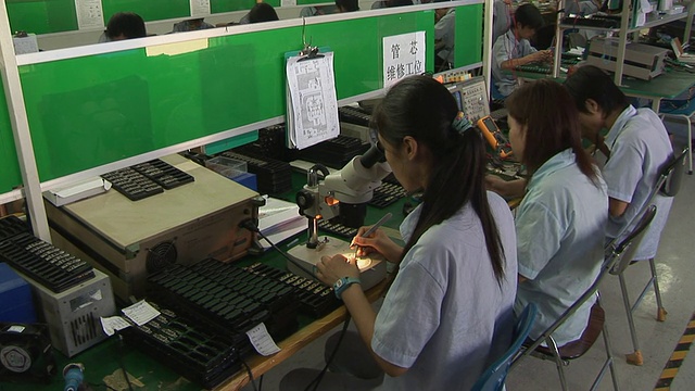 ZI女士的工厂工人坐在桌子前用显微镜组装小零件/中国深圳视频素材