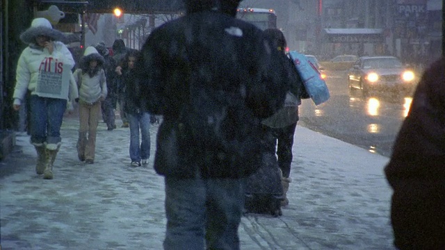 宽阔的镜头后视图的女人拖着行李通过雪和其他行人在人行道/纽约视频素材